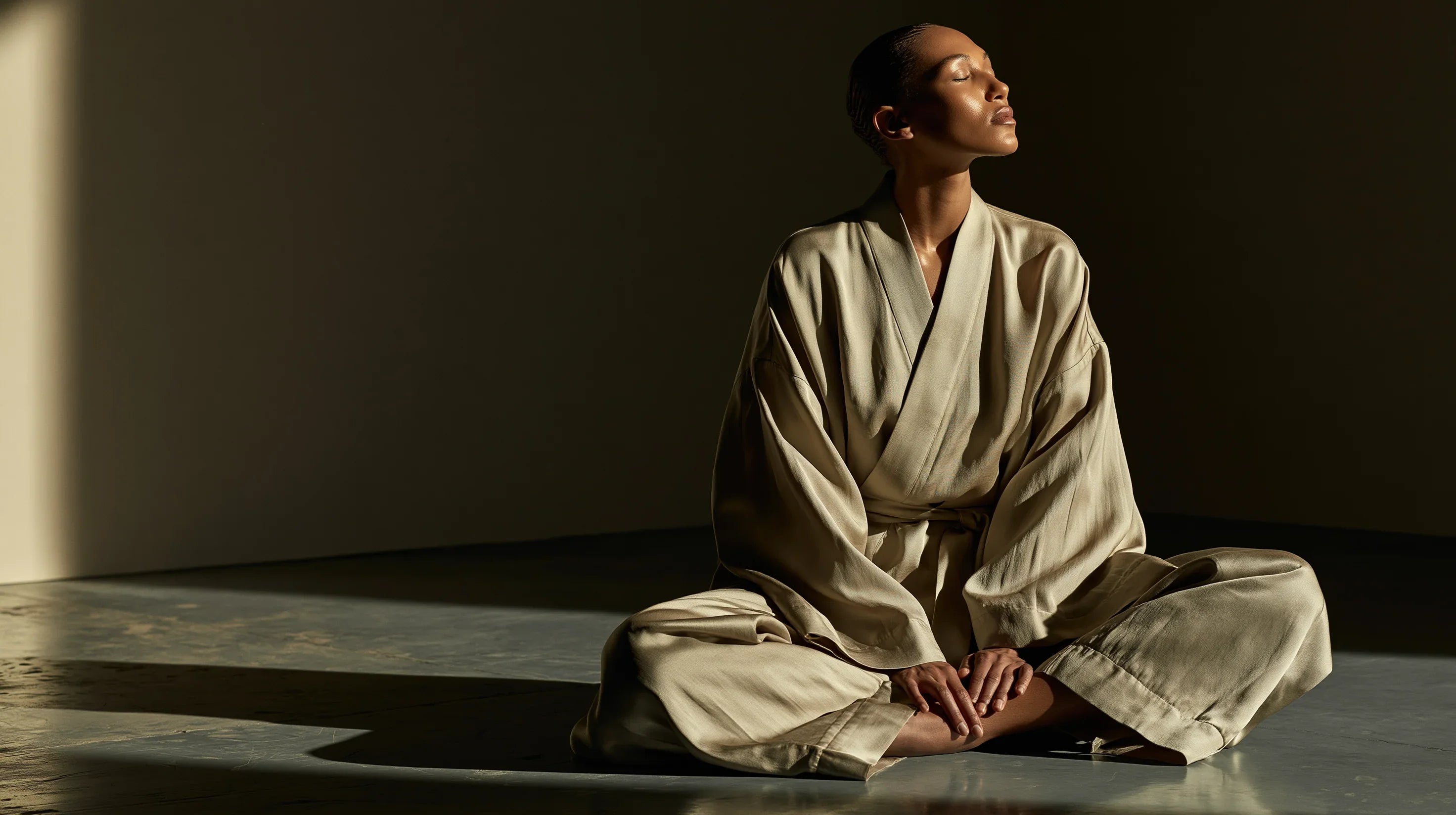 Model in a light robe seated in a calm wellness setting with warm natural light for a FATLAB body care ritual banner